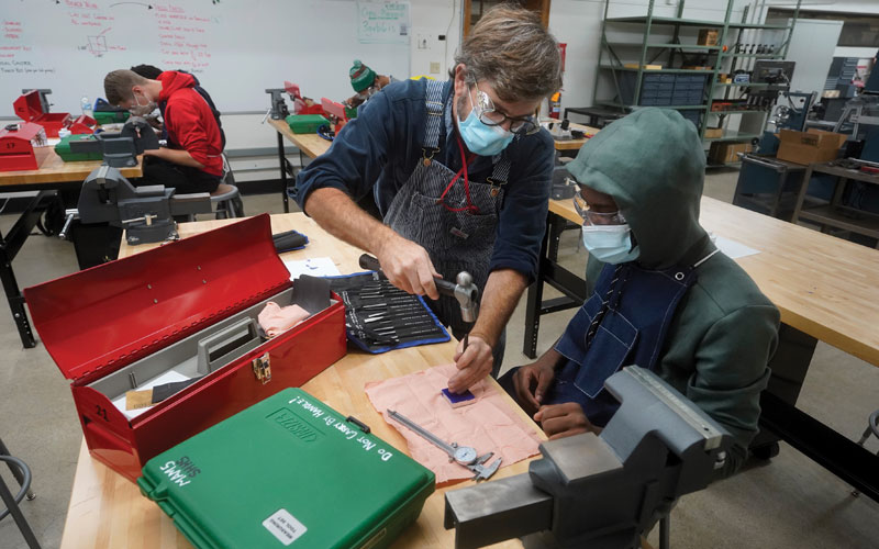 Machining and manufacturing teacher Marty McGuan shows senior Aaron Witt how to mark the center of an aluminum block before drilling.