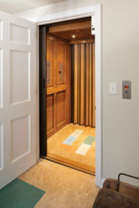  The two-story elevator opens to the garage, stopping in the mudroom and second floor dressing room. The trip from the garage to the mudroom is a short one, covering only a foot. But the return is big – it eliminates the time consuming and physical task of moving a ramp into position each time a wheelchair needs to enter the house from the garage. The flooring is melamine, which is durable and soft and is patterned after the stone colors in the home’s main entryway. 